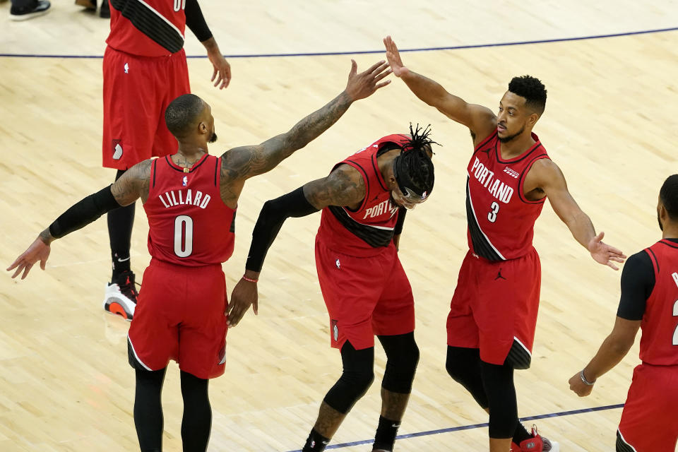 Portland Trail Blazers guard Damian Lillard (0) high fives guard CJ McCollum (3) over forward Robert Covington during the second half of an NBA basketball game against the Phoenix Suns, Thursday, May 13, 2021, in Phoenix. (AP Photo/Matt York)