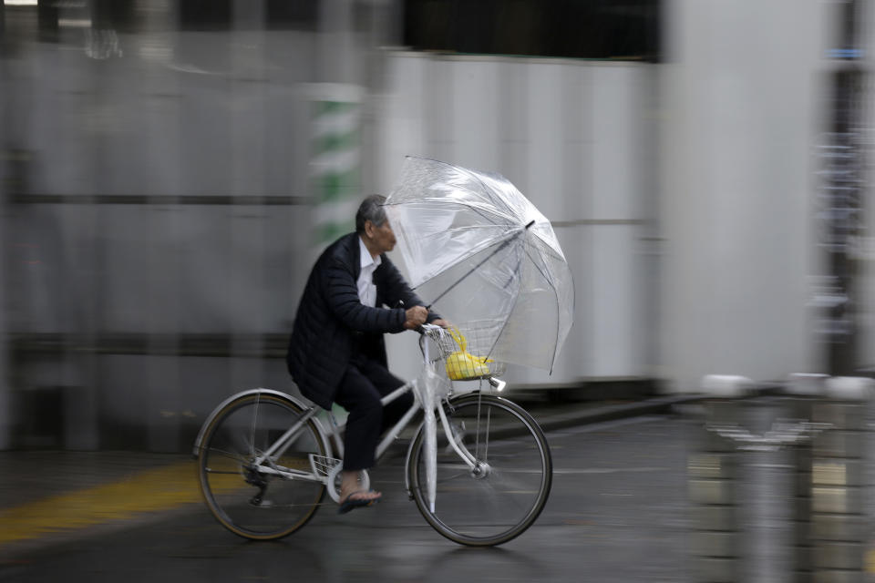 A man holds an umbrella while ride his bicycle in rain in Shibuya district, Tokyo Saturday, Oct. 12, 2019. Tokyo as surrounding areas braced for a powerful typhoon forecast as the worst in six decades, with streets and trains stations unusually quiet Saturday as rain poured over the city. (AP Photo/Kiichiro Sato)