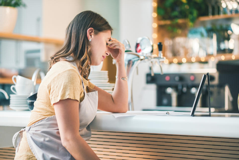 Shot of a young woman experiencing stress while working in a cafe