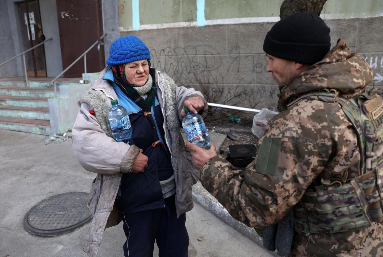 A Ukrainian serviceman gives food and water to a local elderly woman in the town of Bakhmut, in the Donetsk region on 3 March 2023 (AFP via Getty Images)