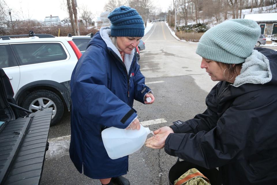 Dippers Tricia Monaghan of Eliot, left, and Amy Clark of York use hot water from a jug to help restore warmth to their hands after being in the Atlantic Ocean at York Harbor on Jan. 19, 2024. Monaghan says she had 157 dips last year.