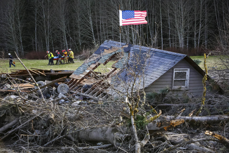 Rescue workers remove a body from the wreckage of homes destroyed by a mudslide near Oso, Wash, Monday, March 24, 2014. The search for survivors of Saturday's deadly mudslide grew Monday to include scores of people who were still unaccounted for as the death toll from the wall of trees, rocks and debris that swept through the rural community rose to at least 14. (AP Photo/seattlepi.com, Joshua Trujillo)