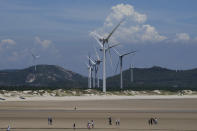 Beachgoers walk near wind turbines along the coast of Pingtan in Southern China's Fujian province on Aug. 6, 2022. The world's two biggest emitters of greenhouse gases are sparring on Twitter over climate policy, with China asking if the U.S. can deliver on the landmark climate legislation signed into law by President Joe Biden this week. (AP Photo/Ng Han Guan)