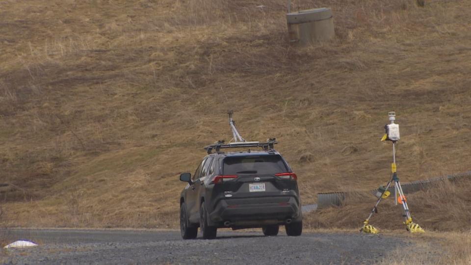 The Flux Lab’s SUV carrying detection equipment drives toward a capped concrete methane well. Beside the car is a stationary methane sensor placed by the measurement team.