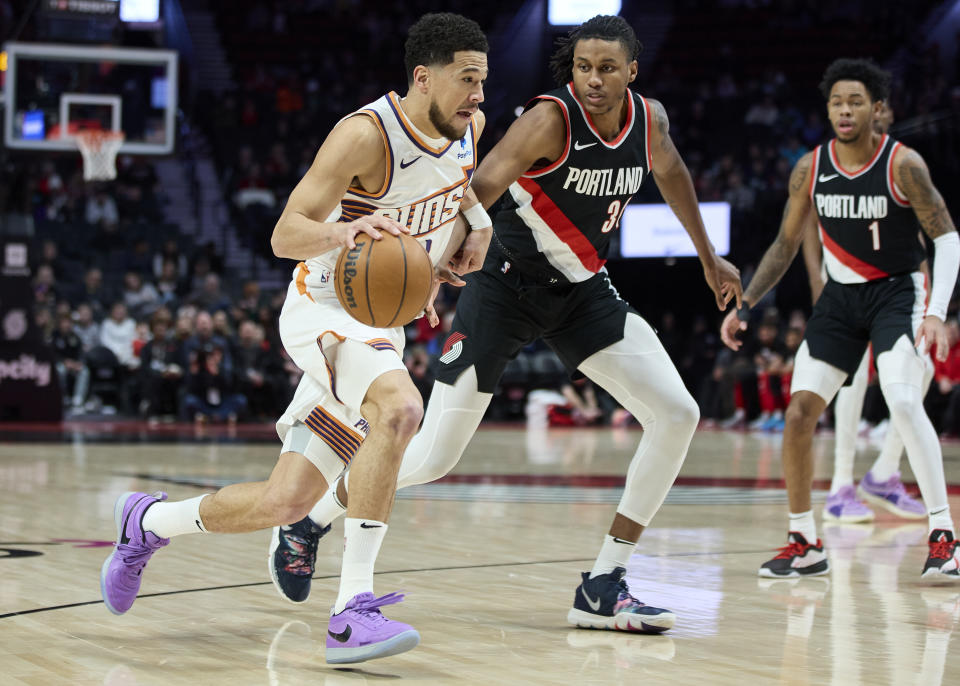 Phoenix Suns guard Devin Booker, left, dribbles past Portland Trail Blazers forward Jabari Walker, center, during the first half of an NBA basketball game in Portland, Ore., Sunday, Jan. 14, 2024. (AP Photo/Craig Mitchelldyer)