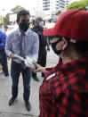 Miami Mayor Francis Suarez, rear, hands out masks to prevent the spread of the new coronavirus, at a mask distribution event, Friday, June 26, 2020, in a COVID-19 hotspot of the Little Havana neighborhood of Miami. Florida banned alcohol consumption at its bars Friday as its daily confirmed coronavirus cases neared 9,000, a new record that is almost double the previous mark set just two days ago. (AP Photo/Wilfredo Lee)