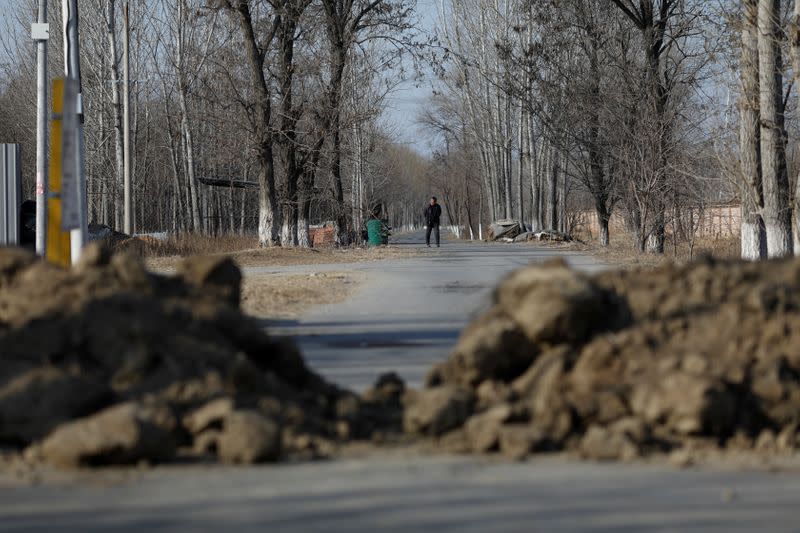 A man walks on a street towards piles of soil blocking the road to prevent outsiders from entering the community, as the country is hit by an outbreak of the new coronavirus, on the outskirts of Beijing