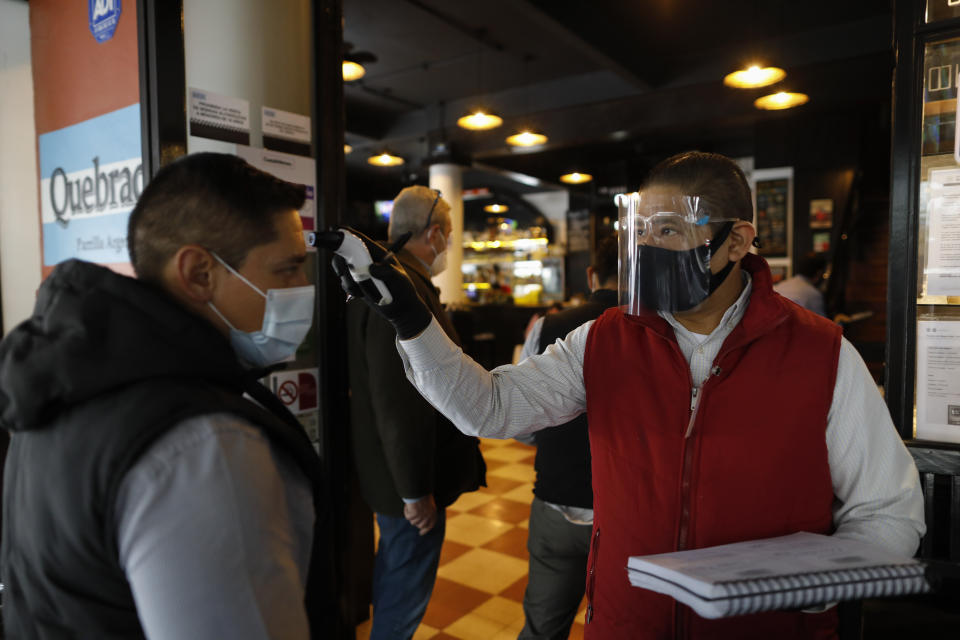 An employee takes the temperature of a diner arriving for lunch at Argentine grill Quebracho, in the Cuauhtemoc neighborhood of Mexico City, Monday, Jan. 11, 2021. More than three weeks into Mexico City's second pandemic shutdown some restaurateurs worried about their ability to survive ignored official warnings and opened limited seating Monday under the slogan "Abrir o Morir," Spanish for "Open or Die." (AP Photo/Rebecca Blackwell)