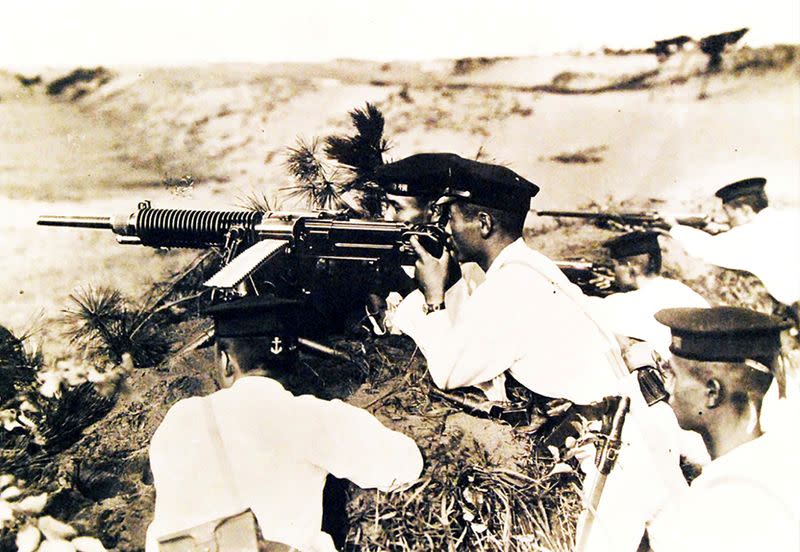 FILE PHOTO: Japanese soldiers wearing white uniforms and dress caps pose behind a heavy machine gun on Guadalcanal