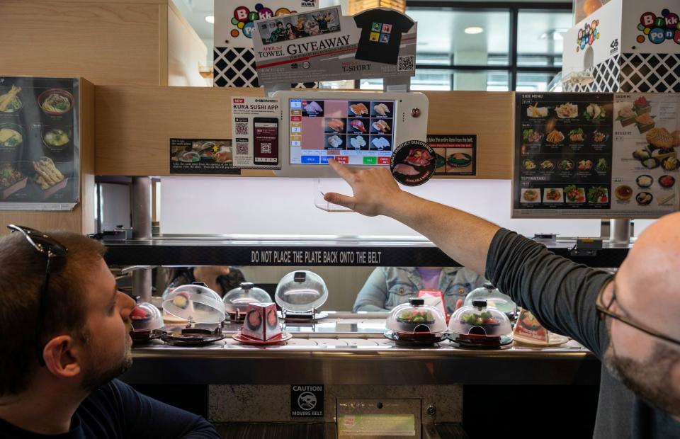 Eddie D. Woodworth left, and Keith Schonberger look through the food menu inside the Kura Revolving Sushi Bar in Troy on April 19, 2023.