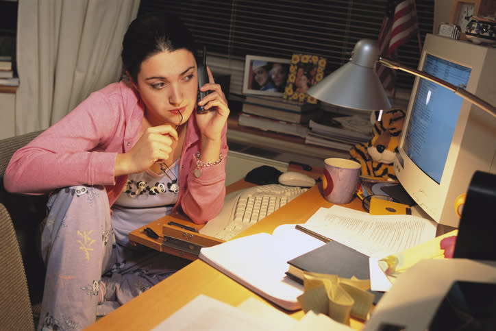 Woman in a casual pink outfit sitting at a desk with a computer, phone to ear, looking thoughtful