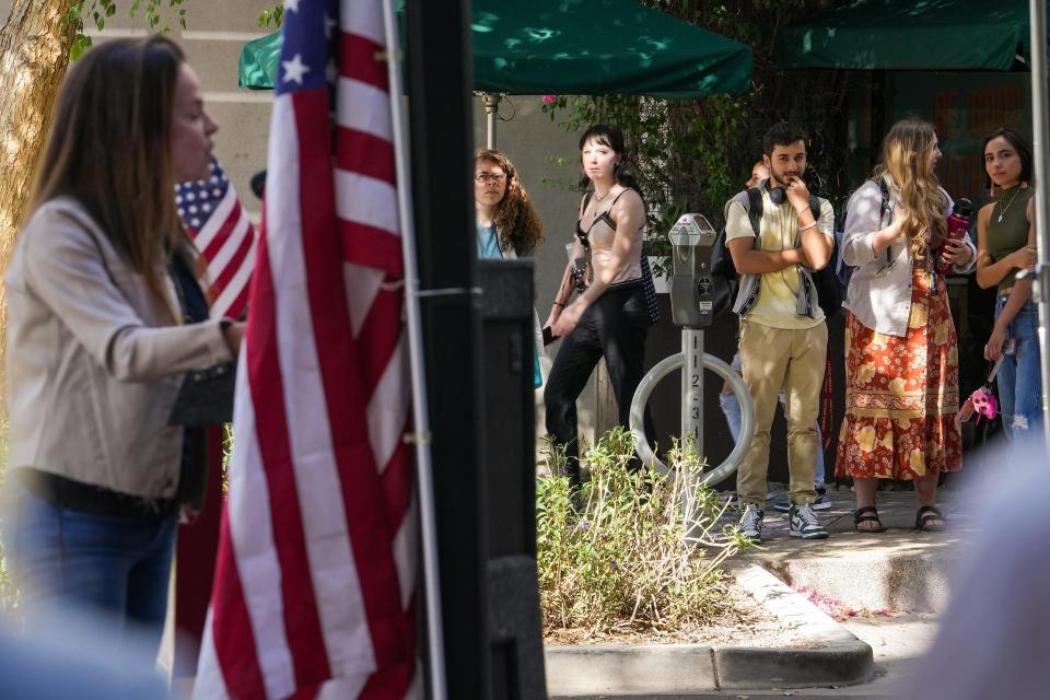 Passersby listen as Marlene Galan-Woods, a former journalists, at left, speaks to media during a press conference at the Arizona State University Downtown Phoenix Campus on Wednesday, Oct. 19, 2022, in Phoenix.