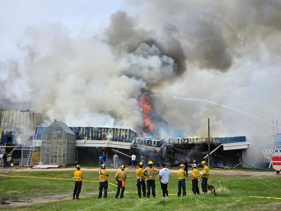 Some firefighters stand watching as others spray water on the burning school at Waterhen Lake First Nation, about 75 kilometres north of Meadow Lake.