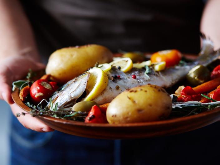 A man holding a plate of fish, potatoes and tomatoes.