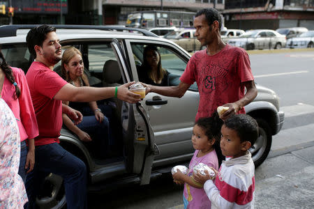 Diego Prada (L), a volunteer of the Make The Difference (Haz La Diferencia) charity initiative, gives a cup of soup and an arepa to a man in a street of Caracas, Venezuela March12, 2017. REUTERS/Marco Bello