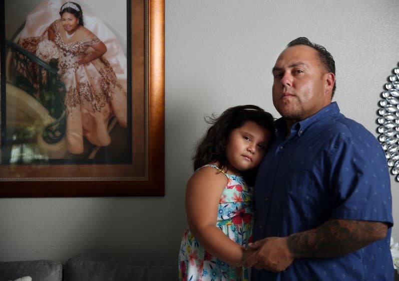LOS ANGELES, CA - JULY 14: Rafael Saaverdra poses for a portrait with his daughter Gianna, 5, and a framed picture of his oldest daughter Gizzelle, 16, hangs beside them in Alhambra on Tuesday, July 14, 2020 in Los Angeles, CA. Saaverdra handles shipping containers from overseas and says that his worst fear is infecting his two daughters with the COVID-19. (Dania Maxwell / Los Angeles Times)