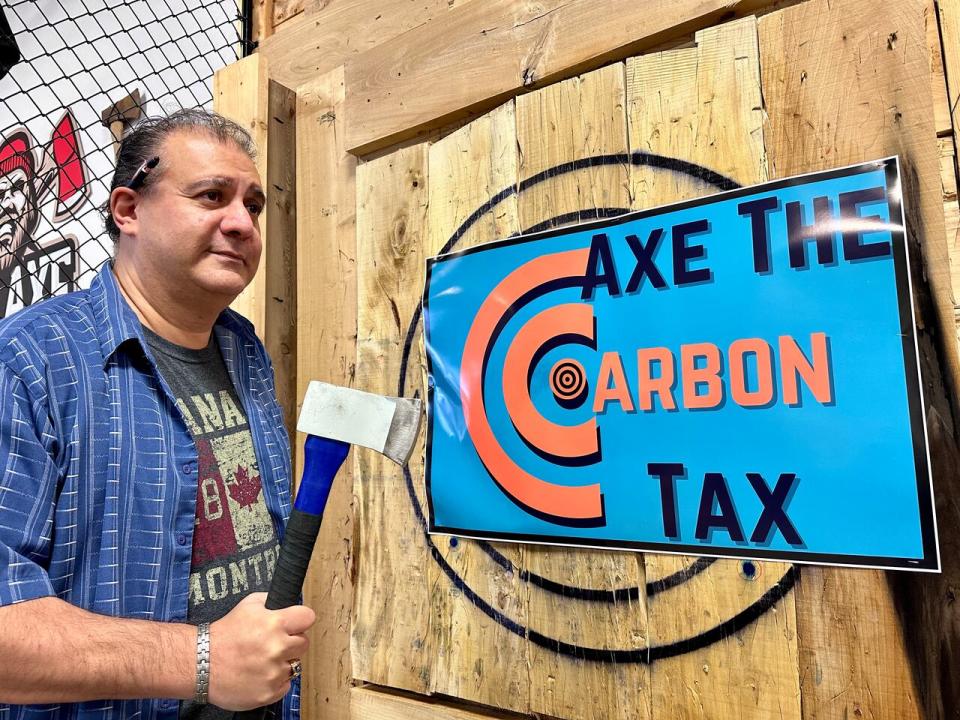 Al Teshuba, president of the Conservative Party's association for Windsor West, holds an axe next to a custom target at Bad Axe Throwing on Dougall Avenue in Windsor. (Dalson Chen/CBC - image credit)