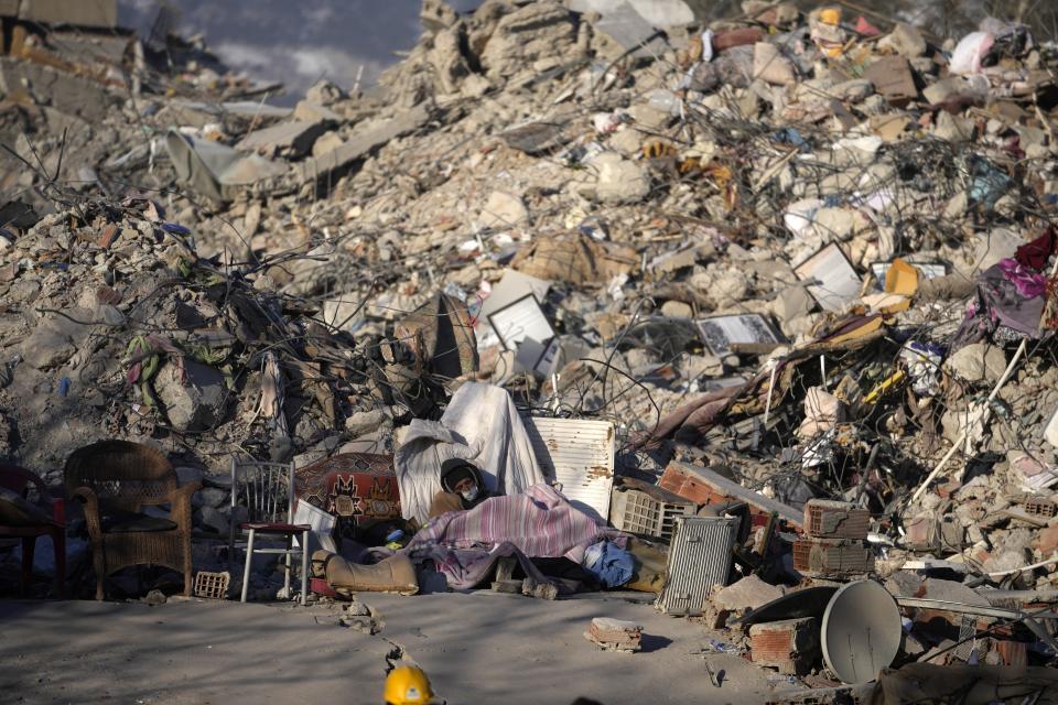 A man sleeps in front of a destroyed building in Kahramanmaras, southeastern Turkey, Monday, Feb. 13, 2023. Thousands left homeless by a massive earthquake that struck Turkey and Syria a week ago packed into crowded tents or lined up in the streets for hot meals Monday, while the desperate search for anyone still alive likely entered its last hours. (AP Photo/Khalil Hamra)