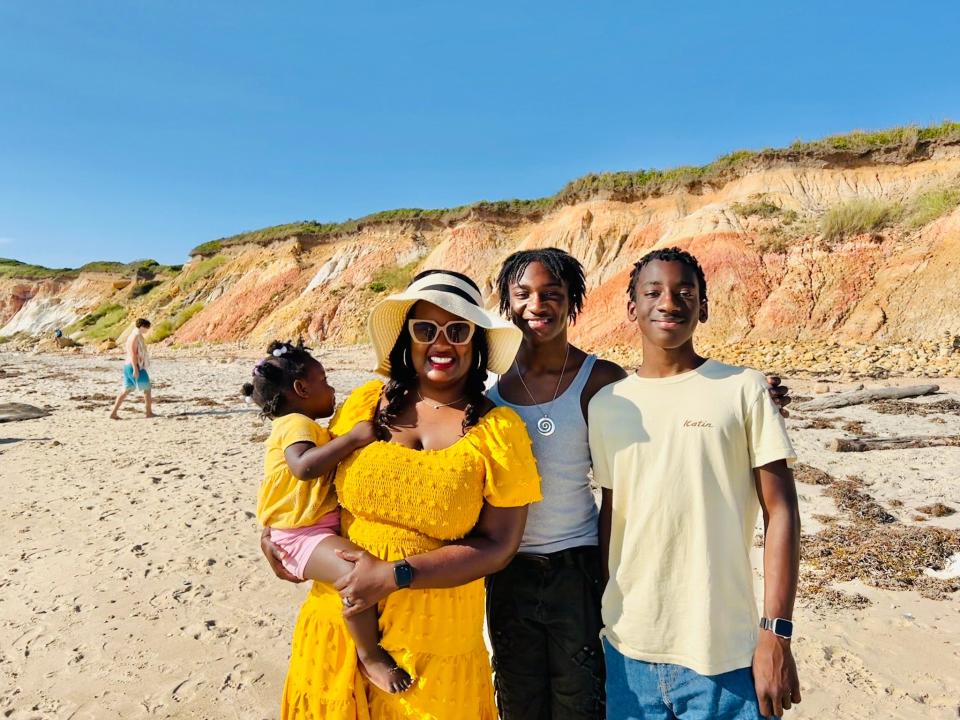 Amanda Miller Littlejohn with her sons and daughter at the beach, they are smiling in the sun and standing on the sand.