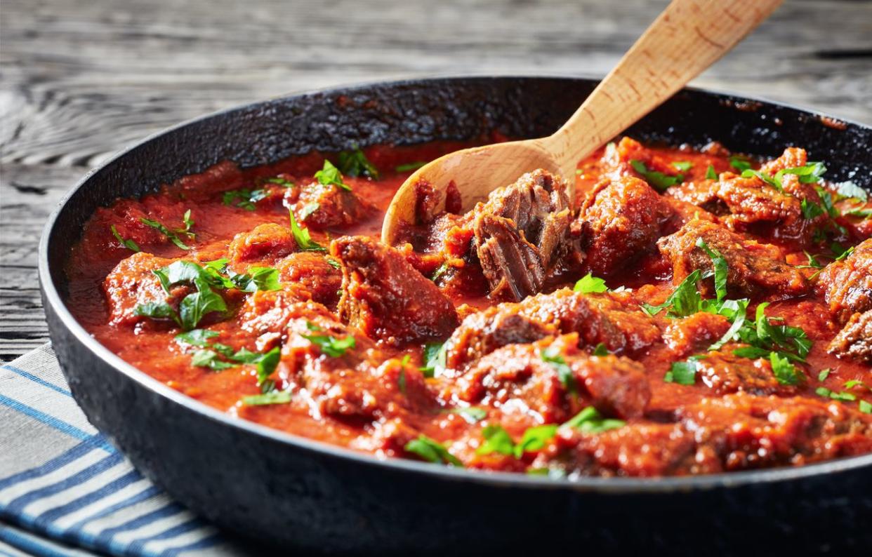 lose-up of spicy Beef Stew in tomato sauce with spices and herbs in a skillet on a rustic wooden table, west African cuisine