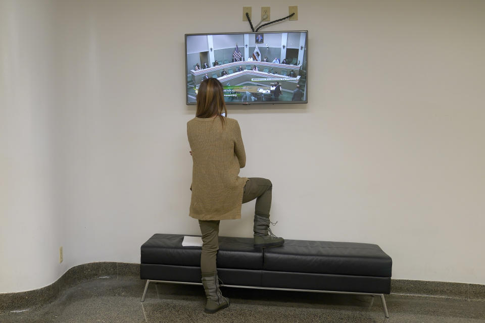 Sara Dutt watches a hearing of the Assembly Health Committee, outside the hearing room at the Capitol in Sacramento, Calif., Tuesday, Jan. 11, 2022. Dutt joined others in appearing before the committee to speak in opposition of a measure by Assemblyman Ash Kalra, D-San Jose, to create a universal health care system. Due to COVID-19 restrictions Dutt had to wait to appear before the committee. (AP Photo/Rich Pedroncelli)