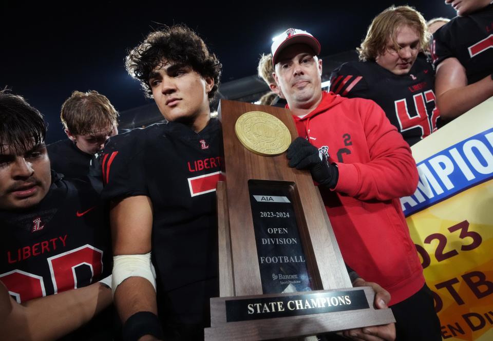 Liberty head coach Colin Thomas and quarterback Navi Bruzon (7) hold their trophy to celebrate their 33-21 win over Centennial for the Open Division State Championship at Mountain America Stadium in Tempe on Dec. 2, 2023.