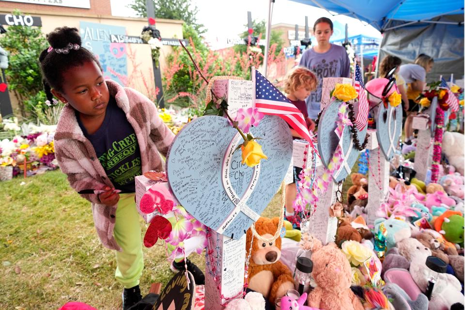 London M., of Allen, Texas, whose mother asked to only use her initial for her last name, signs a cross after signing all the others at a makeshift memorial by the mall where several people were recently killed, Wednesday, May 10, 2023, in Allen, Texas. 