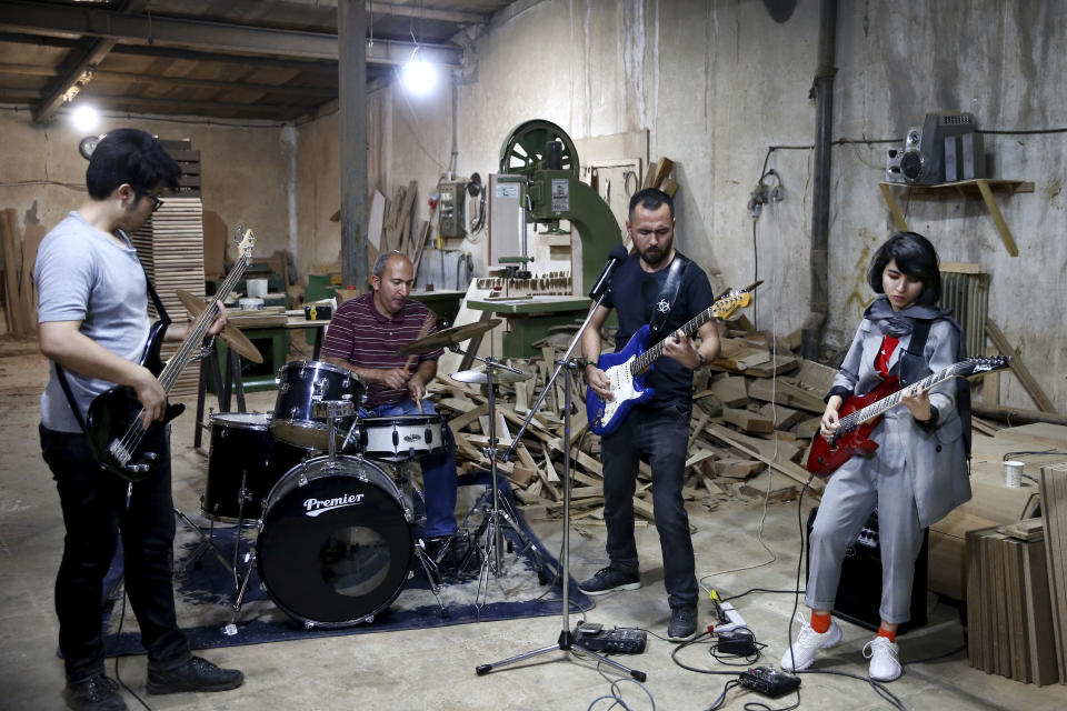 In this July 20, 2018 photo, Afghan musicians Mohammad Rezai, left, Hakim Ebrahimi, second right, and Soraya Hosseini, right, members of the Arikayn rock band, along with Kourosh Ghasemi, an Iranian drummer, play music at a furniture workshop in Eslamshahr, outside Tehran, Iran. Like others in Iran's vibrant arts scene, Afghan musicians must contend with hard-liners who view Western culture as corrupt and object to women performing in public. (AP Photo/Ebrahim Noroozi)
