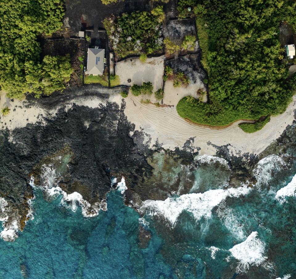 Travelers planning to visit Hawaii during the holidays should decide their means of transportation well ahead of time.
Pictured: a coast of Hawaii with roaring waves and lush green forests surrounding a residential area on the beach 