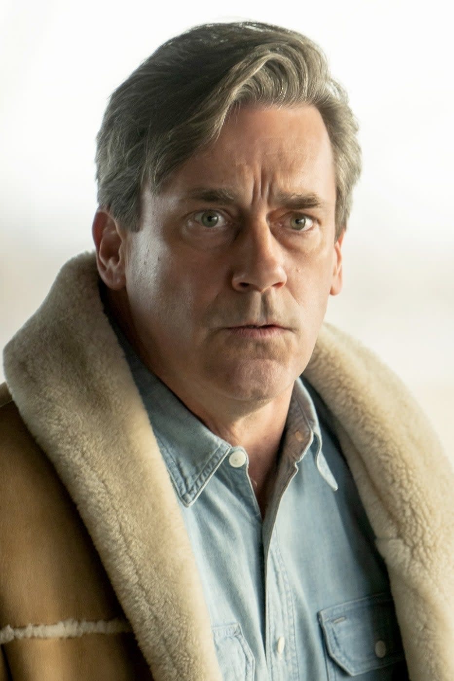 Jon Hamm wears a shearling-lined jacket over a denim shirt in a serious scene from a TV show