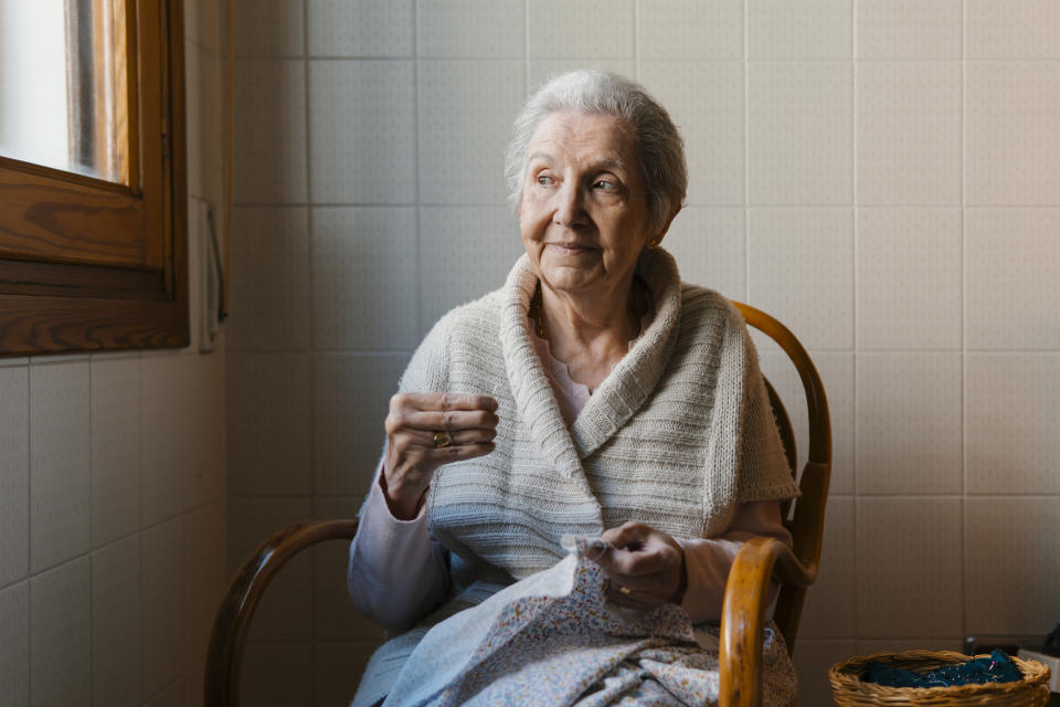 An older woman smiling as she sits and sews