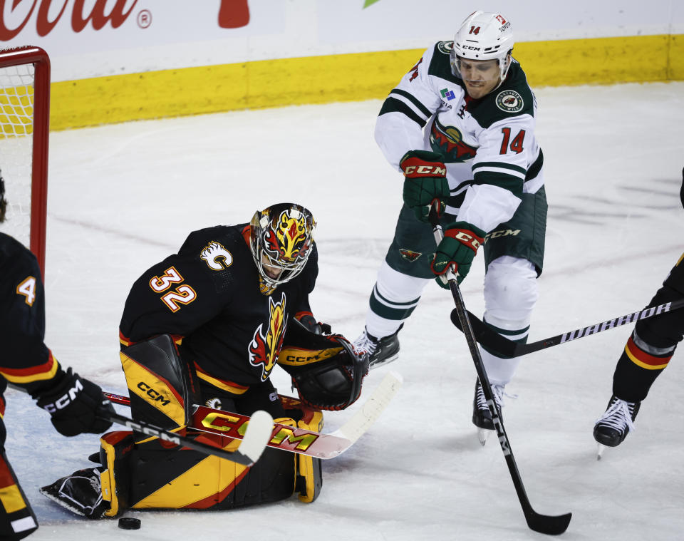 Minnesota Wild forward Joel Eriksson Ek, right, has his shot kicked away by Calgary Flames goalie Dustin Wolf during the second period of an NHL hockey game, Tuesday, Dec. 5, 2023 in Calgary, Alberta. (Jeff McIntosh/The Canadian Press via AP)