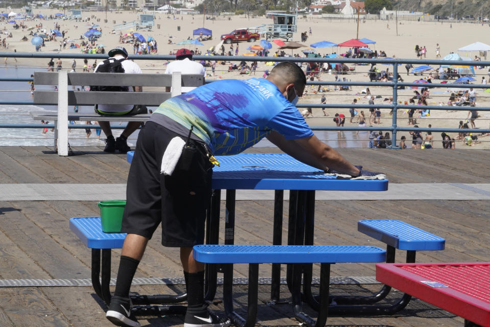 Pacific Park worker Roberto Gil sanitizes tables and benches ahead of opening on April 1 opening of the amusement park on the Santa Monica Pier in Santa Monica, Calif., Wednesday, March 31, 2021. Health officials in California and across the country are urging caution because of a troubling rise in new cases of COVID-19, but aquariums and amusement parks are on track to reopen in California anyway. (AP Photo/Damian Dovarganes)