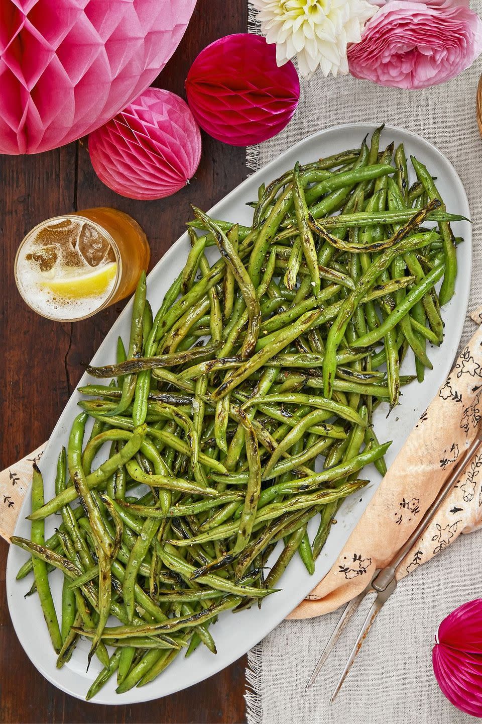 salt and pepper charred green beans on a long white oval serving plate with a serving utensil