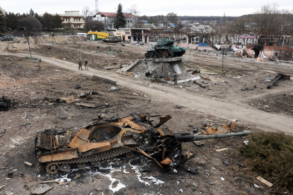 Local residents pass by a damaged Russian tank in the town of Trostyanets, east of capital Kyiv, Ukraine, Monday, March 28, 2022. The monument to Second World War is seen in background. (AP Photo/Efrem Lukatsky)