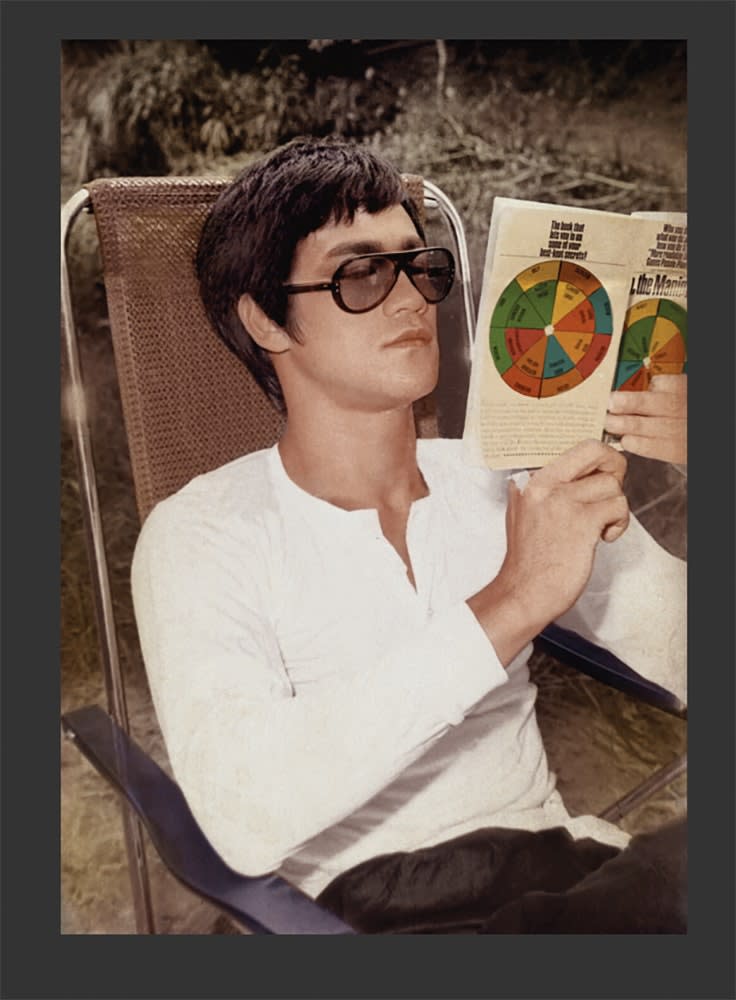 Bruce Lee reading a book from a chair