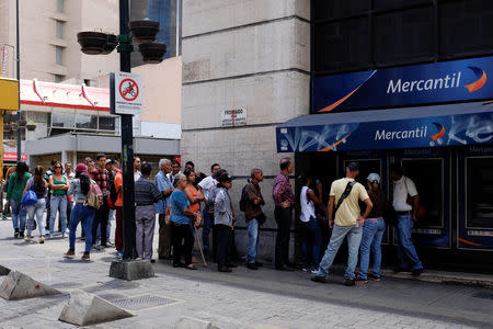 People line up to withdraw cash from an automated teller machine (ATM) outside a Banco Mercantil branch in Caracas, Venezuela August 17, 2018. REUTERS/Marco Bello