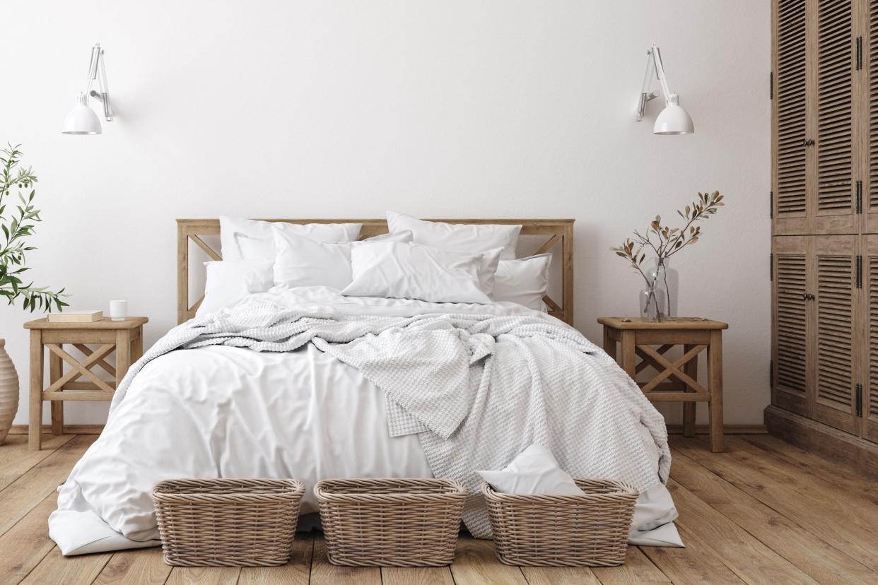 Queen bed with white sheets and duvet cover with three baskets framing edge, foot of the bed, two matching nightstands on both sides, with a matching headboard, plant decorations, and a rustic and simple vibe, on a wooden floor
