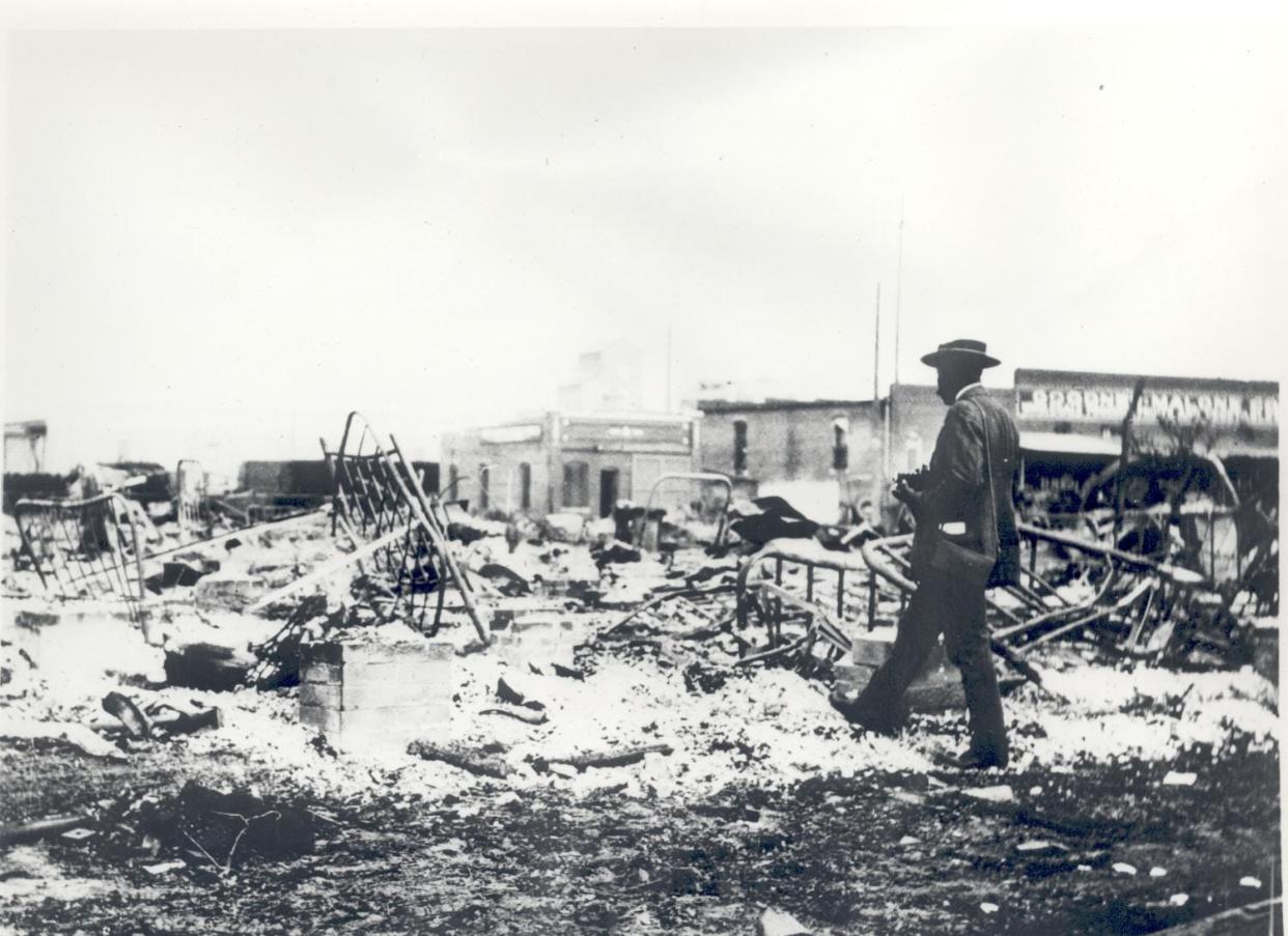 Photograph of an African-American man with a camera looking at the skeletons of iron beds which rise above the ashes of a burned out block after the Tulsa Race Massacre, June 1, 1921. Courtesy of the Oklahoma Historical Society