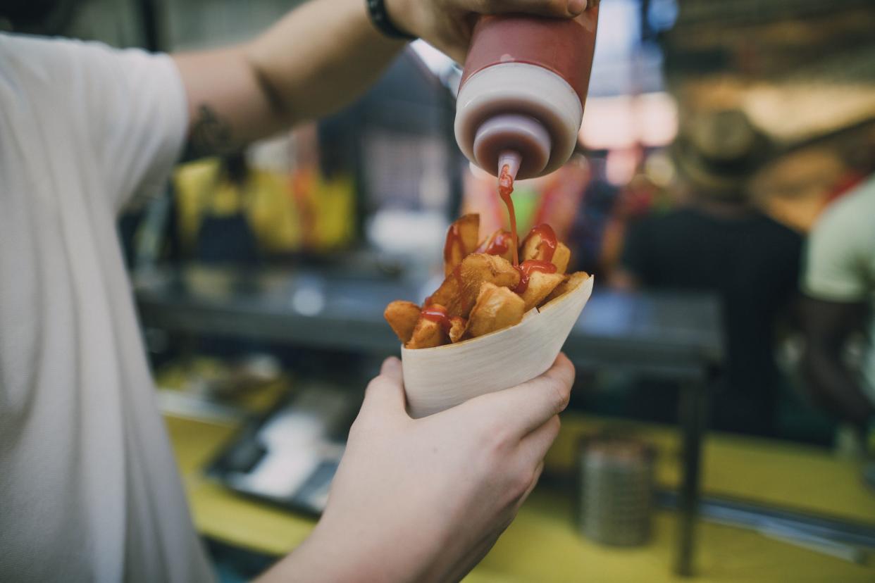 Close up shot of a man getting chips from a stall in Queen Victoria Market, Australia. He is squirting ketchup on them.