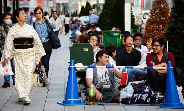 A woman wearing kimono walks beside people sitting down as they queue in front of an Apple Store at Ginza shopping district to wait for the new iPhone 5s and 5c in Tokyo on September 19, 2013, a day before Apple's new smart phone will go on sale