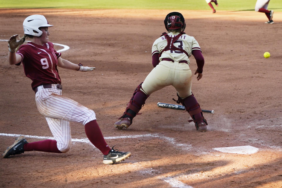 Alabama's Taylor Clark (9) slides safely behind Florida State catcher Anna Shelnutt (13) to score in the third inning of an NCAA Women's College World Series softball game Monday, June 7, 2021, in Oklahoma City. (AP Photo/Sue Ogrocki)