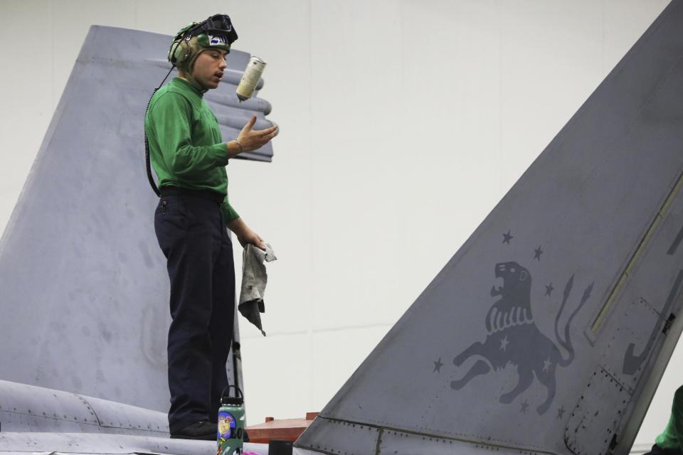 In this Tuesday, March 21, 2017 photograph, a sailor tosses a spray can in the air while working on an F-18 fighter jet on the USS George H.W. Bush as it travels through the Strait of Hormuz. The arrival of the nuclear-powered aircraft carrier to the Persian Gulf marks the first such deployment under new U.S. President Donald Trump. (AP Photo/Jon Gambrell)