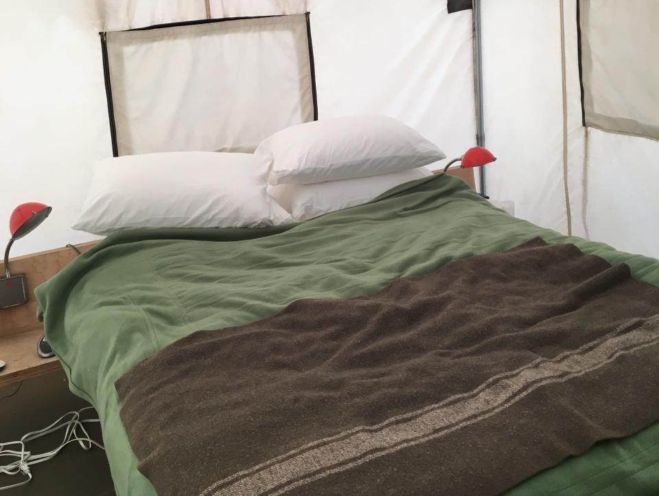 A double bed inside of a tent with a green and brown blankets.