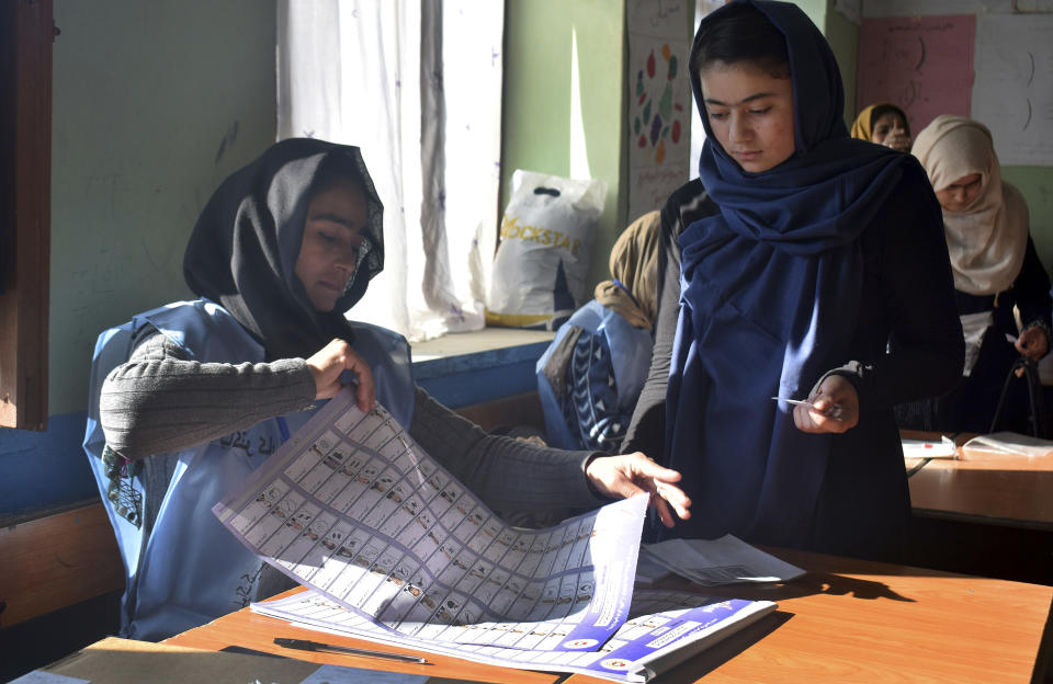In this Saturday, Oct. 20, 2018, photo, an employee of Independent Elections Commission, left, prepares a ballot paper for a young female voter before casting her vote at a polling station in Faizabad, center of northern Badakhshan province, Afghanistan’s parliamentary elections entered a second day on Sunday, Oct. 21, 2018, following violence and chaos that caused delays and interruptions on the first day of polling. (AP Photo/Omer Abrar)