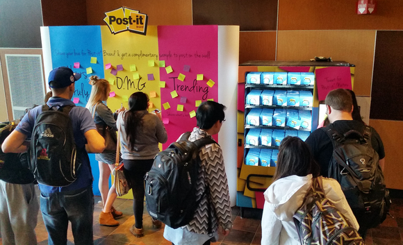 People in front of a multi-colored Post-it board with various messages.