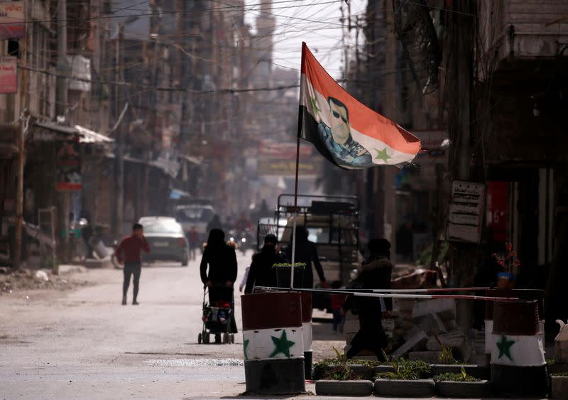 FILE PHOTO: A national flag depicting a picture of Syria's President Bashar al-Assad flutters at a checkpoint in Douma