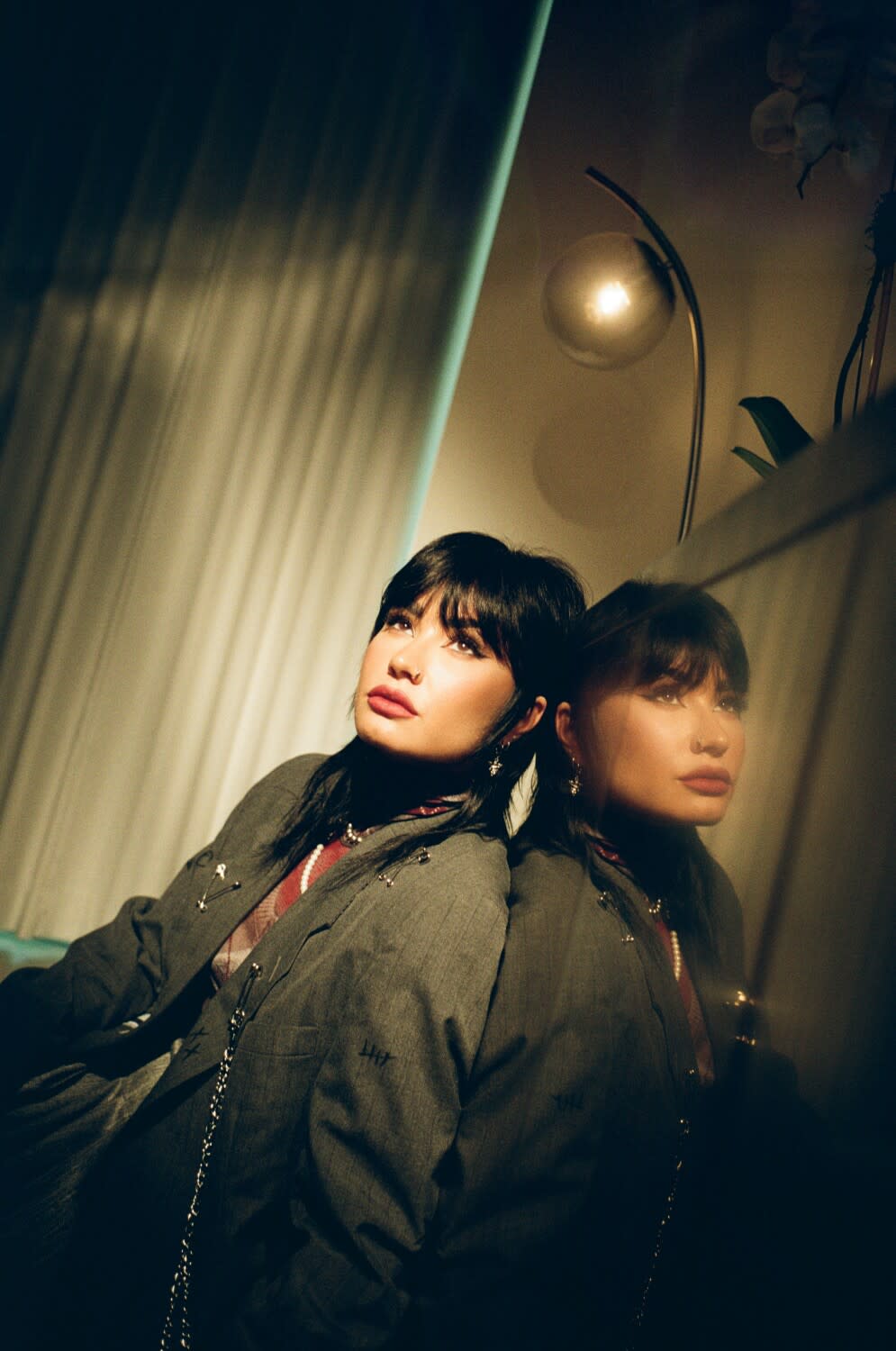 A woman, seated on the floor, poses for a photograph, alongside her reflection