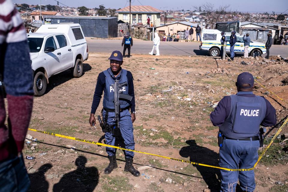 South African Police Service (SAPS) officers enforce a perimeter around a crime scene as investigators inspect the crime scene where 15 people where shot dead in a tavern as a forensic team investigates in Soweto on July 10, 2022.