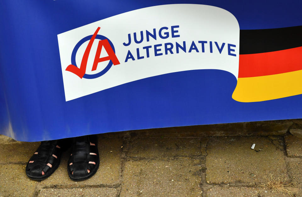 Ein Mann in schwarzen Sandalen hält ein Plakat der AfD-Jugendorganisation Junge Alternative (JA). (Bild: Jens Kalaene/zb/dpa)